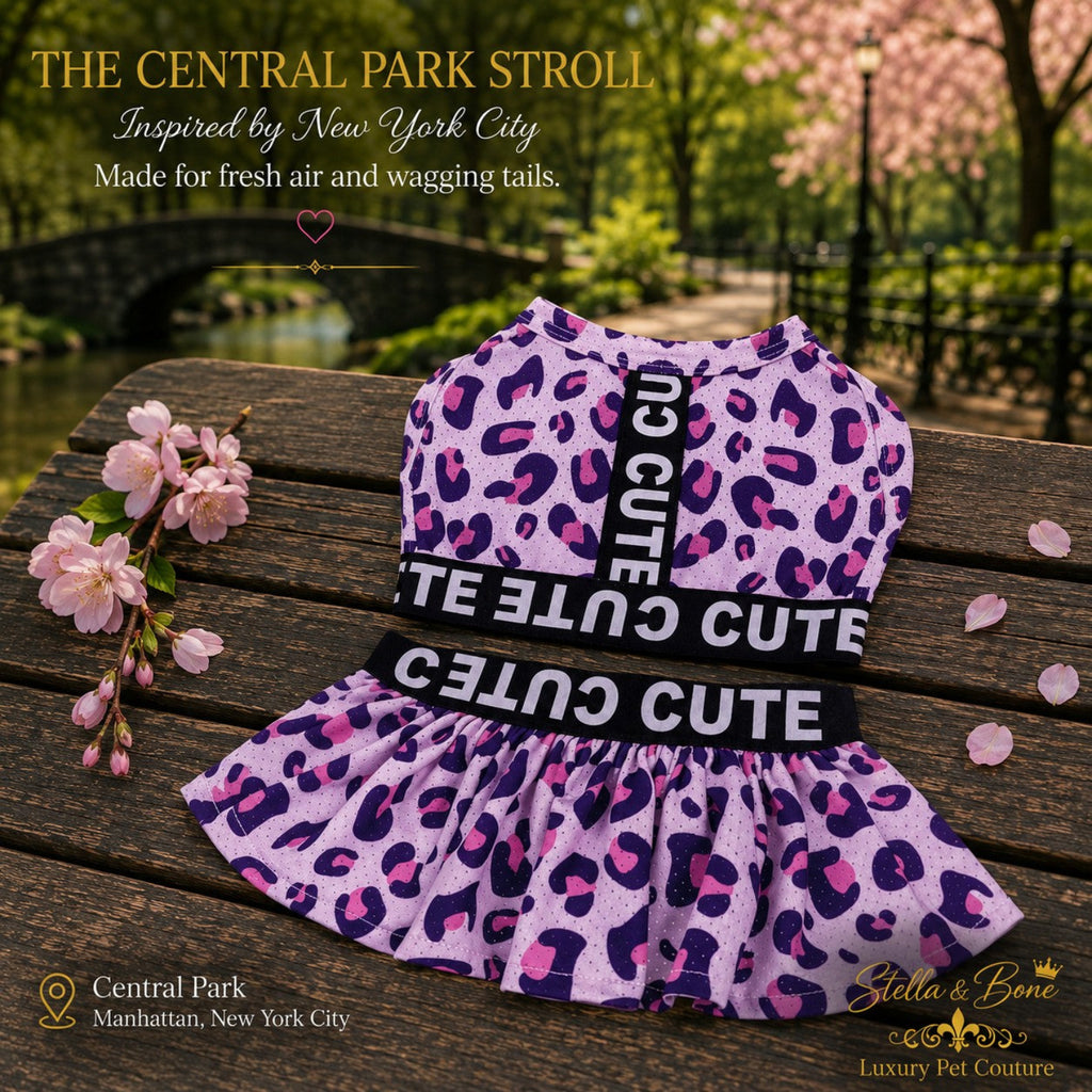 Flat lay view of The Central Park Stroll luxury dog dress in pink leopard print on a wooden bench with cherry blossoms.